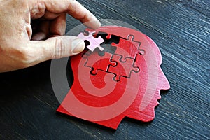 Treating mental illness and memory problems. The hand puts a piece of the puzzle on the shape of the head.