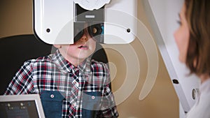 A treatment in eye clinic - checking little boy`s eye vision by looking through big special device with lenses