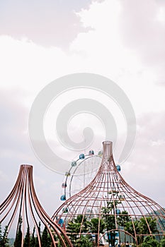 A tree cage and Ferris wheel with a backdrop of slightly cloudy skies