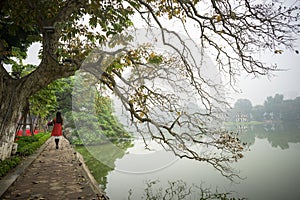 Tree in fall season at Hoan Kiem lake with Vietnamese girl wear traditional dress Ao Dai walking by lake in Hanoi