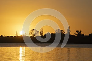 Tree and land silhouette across bay as sunrises