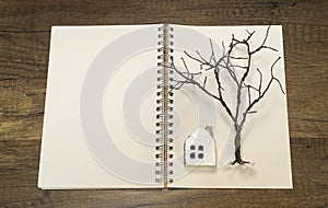 Tree without leaves with white house on white blank notebook