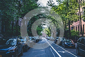 Tree lined street of historic brownstone apartment buildings in West Village neighborhood in Manhattan, New York City. Cars parked