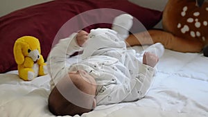 Tree months old baby boy dressed in white, on white quilt kicking with his feet and making funny faces