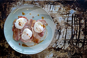 Tree rushes bacon with poached eggs on blue plate, top view
