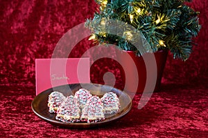 Tree shaped decorated sugar cookies left out for Santa, with a lighted tree, on a red background