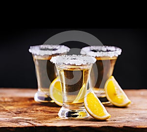 Tree shot glasses of Mexican tequila cocktail with lemon slices and salt on wooden table with black background