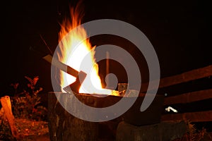 Tree stump with axe and burning firewood in metal brazier outdoors at night