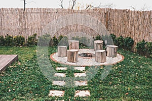 Tree stumps around fire pit with smoke rising from the burning logs. Camping area, cozy backyard fire pit