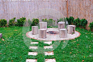 Tree stumps around fire pit with smoke rising from the burning logs. Camping area, cozy backyard fire pit