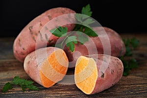 Tree sweet potatoes batatas, one of which is cut into two halves, on the rustic wooden table with black background.