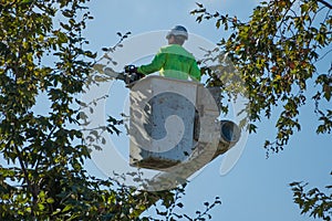 Tree trimmer in bucket holding a chainsaw