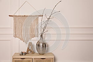 Tree twigs in metal vase and decor on wooden table near white wall. Space for text