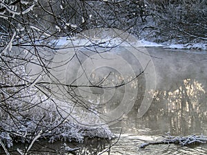 Trees covered with frost near the unfrozen river in winter