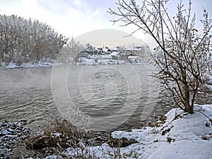 Trees covered with frost near the unfrozen river in winter