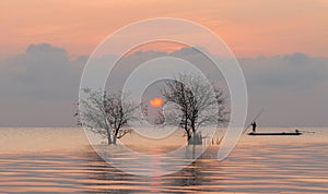 Trees and fisherman in the lake with beautiful sunrise and sky.