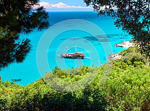 Trees frame beautiful view on amazing island bay with pirate corsair style boat ship, swimming people, beach in Ionian Sea blue wa