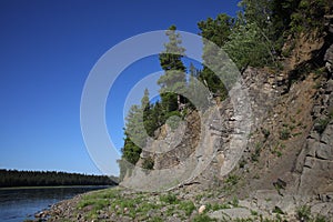 Trees grow on a steep cliff on bare rocks near the river.