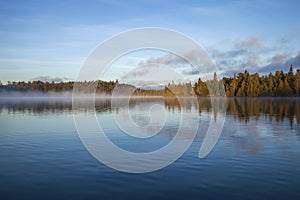 Trees and shoreline in early morning fog and light on a beautiful blue northern Minnesota lake in September