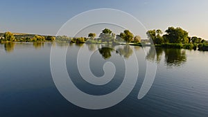 Trees and varios wetland plants on bank of large fish pond, water surface with slight ripples, summer afternoon sunshine photo