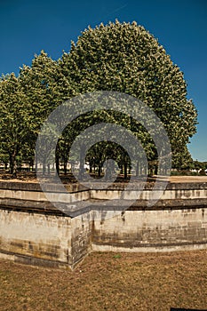 Trees and wall that forms part of the palaceâ€™s moat of Les Invalides in a sunny day at Paris.