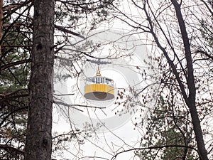 Among the trees you can see a yellow retro cable car cabin against a cloudy sky