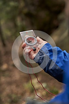 Trekker searching right direction in forest with magnetic compass