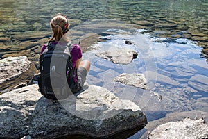 Trekker sitting on a big rock on the shore of a very clear mountain lake