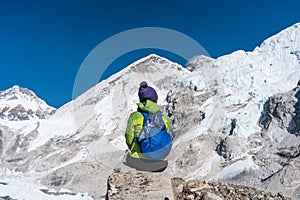 A trekker sitting on rock at Everest base camp surrounded by Himalaya mountains range in Nepal