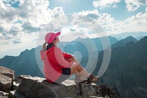 Trekker woman dressed red active people clothes sitting on Rysy peak 2499m enjoying High Tatras mountain range covered mist,