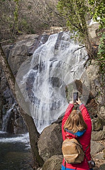 Trekker woman taking pictures with smartphone at Nogaleas waterfall