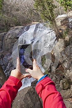 Trekker woman taking pictures with smartphone at Nogaleas waterfall