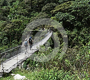 Trekkers crossing a hanging wire bridge.