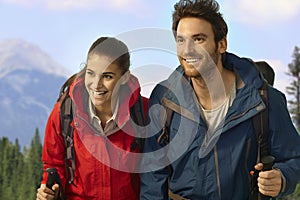 Trekking couple climbing uphill smiling.