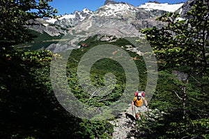 Trekking in Patagonia, Man with big backpack hiking on gray stony path in green forest with view of Jakob lagoon
