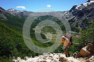 Trekking in Patagonia, Man with big backpack walking up on mountainside with view of green Rucaco valley in Nahuel Huapi