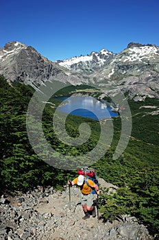 Trekking in Patagonia, Picturesque mountain lake, Man with big backpack hiking uphill on gray stony path in green forest