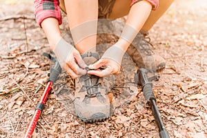 Close up of asian young woman trekking stops and sitting to tie her shoe.