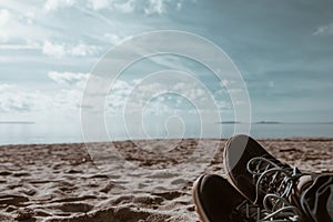 Trekking shoes in the foreground - people taking rest at the beach in a sunny day