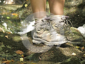 Trekking shoes on women`s legs closeup. Women stands alone on rock near mountain river. Outdoor lifestyle travel concept