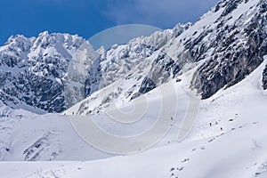 Trekking and skituring in High Tatra Mountains in winter. Trail in snow with people and the giant rocky mountains in the bacground