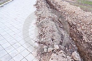 Trench with excavated earth or ground for pipes on sewage in parallel line with the sidewalk for pedestrians in the city street se