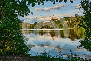 Hrad nad riekou. Pohľad na pravý breh. Orámované listami stromov. Trenčín, Slovensko.