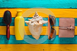 Trend accessories for relaxation on the beach and beauty on a yellow blue wooden table. Purse, comb, sunglasses, shell, sunblock.