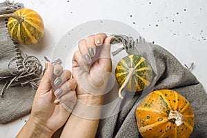 Trend manicure in autumn colors on a gray table next to pumpkins and a gray scarf