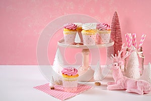 On trend pink Christmas children's party table with cupcakes and holiday decor.