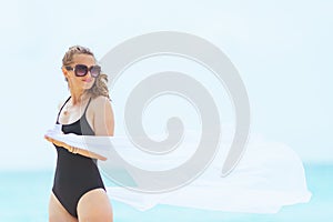 Trendy 40 year old woman on white beach holding white pareo