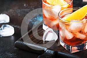 Trendy alcoholic cocktail Negroni with dry gin, red vermouth and red bitter, orange slice and ice cubes. Brown bar counter