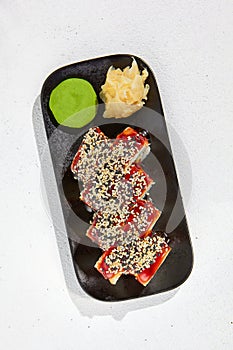 Trendy asian food - canada maki on black plate on white concrete background. Sushi roll with eel and unagi sauce outside, cheese,