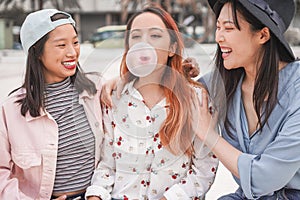 Trendy asian girls having fun together outdoor - Young women friends playing with bubble gum - Trends, youth, millennial
